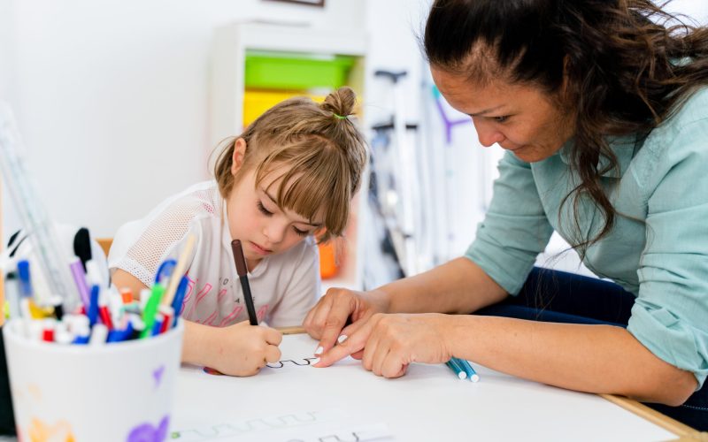 A girl with down syndrome is in a classroom with her teacher